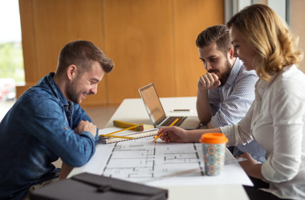 Three designers reviewing kitchen plans with laptops and coffee cups in a design studio – Atlanta design center locations listed