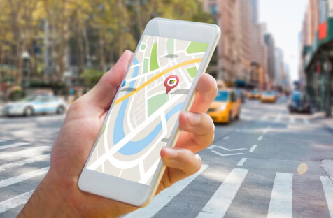 Hand holding smartphone with map and location pin displayed, indicating design center store locator in a busy city street