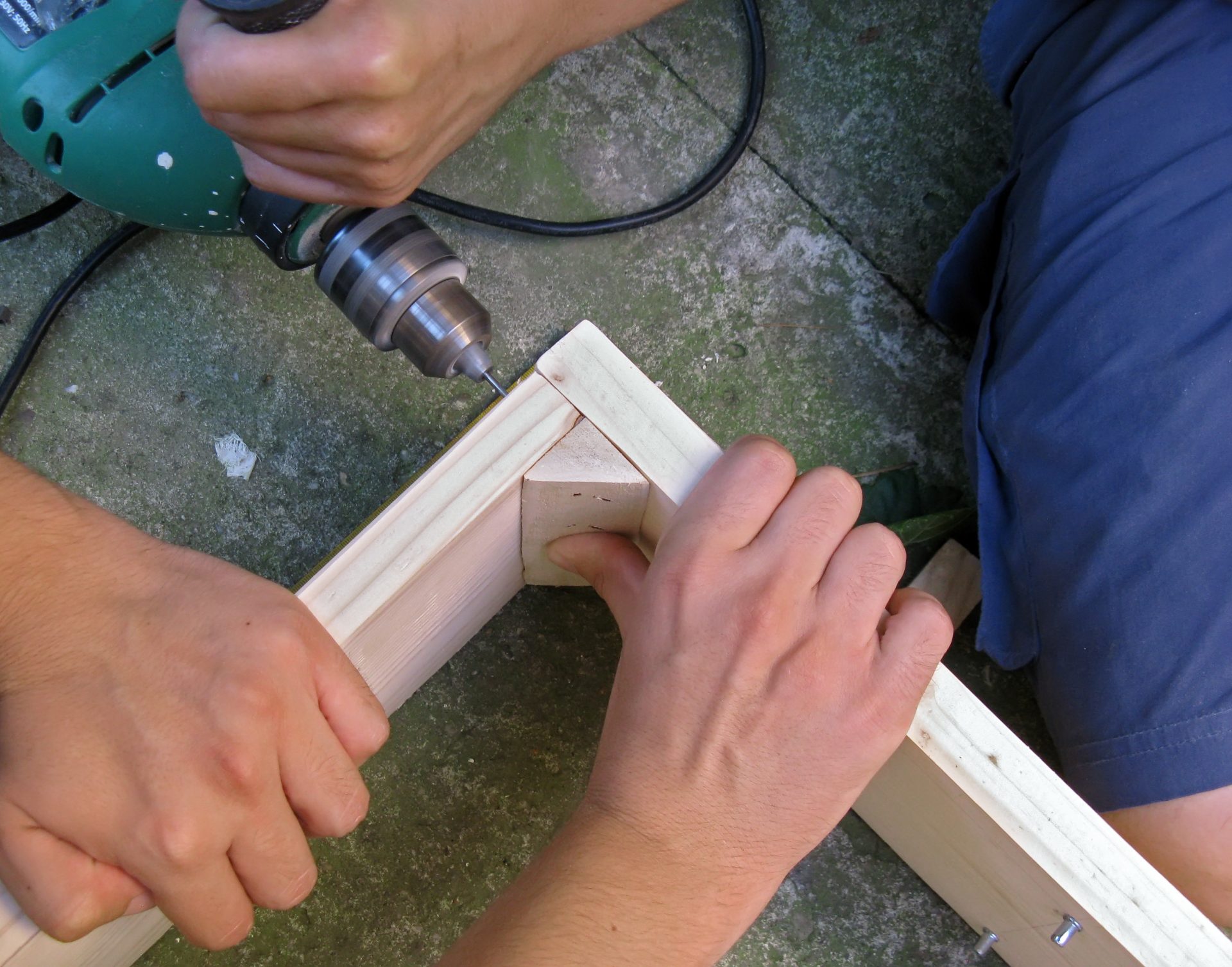 Teamwork - working on building a cabinet. Drilling a hole in wood.