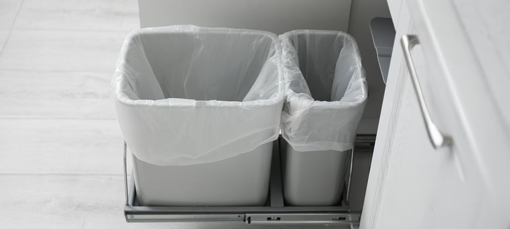 Open kitchen cabinet with pull-out dual trash and recycling bins designed for compact waste management in multi-family units
